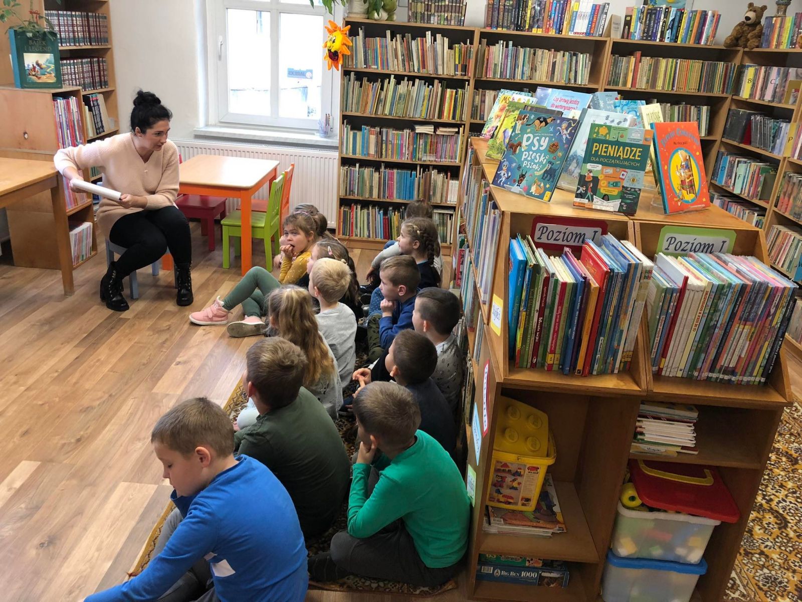 Dzieci siedzące na dywanie słuchają uważnie pani bibliotekarki.