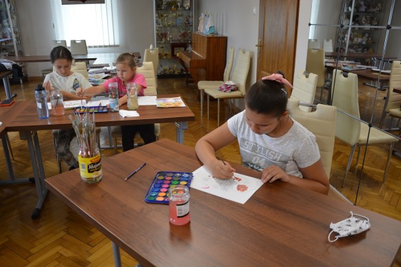 Dziewczynka maluje na stole akwarelami podczas warsztatów plastycznych