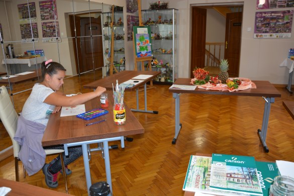 Dziewczynka maluje akwarelami kompozycję owoców na stole